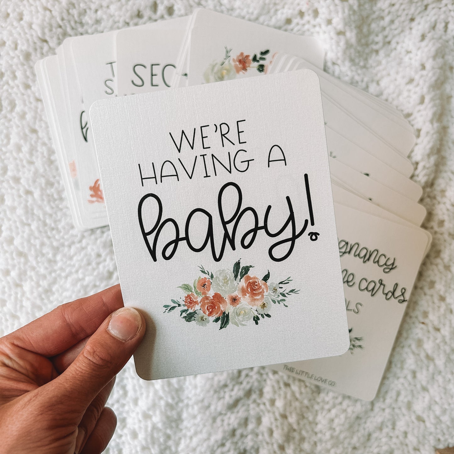 Milestone card reads We're having a baby! in black text with a floral bouquet beneath the text.