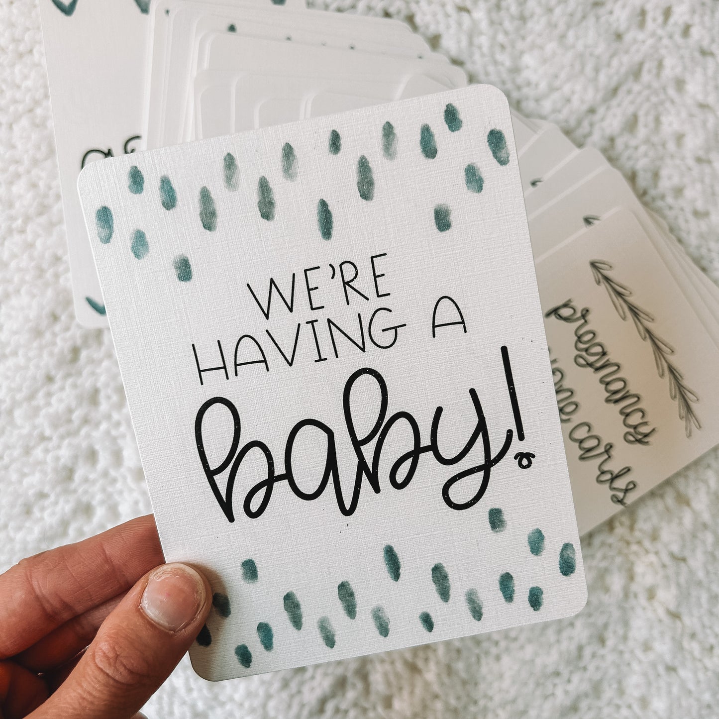 Milestone card reads We're having a baby! in black text with blue dots above and below the text
