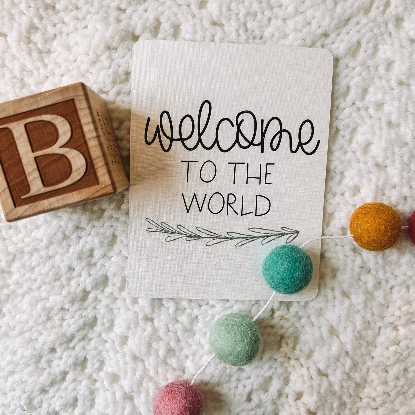 Milestone card reads welcome to the world in black text with a leafed branch beneath it.