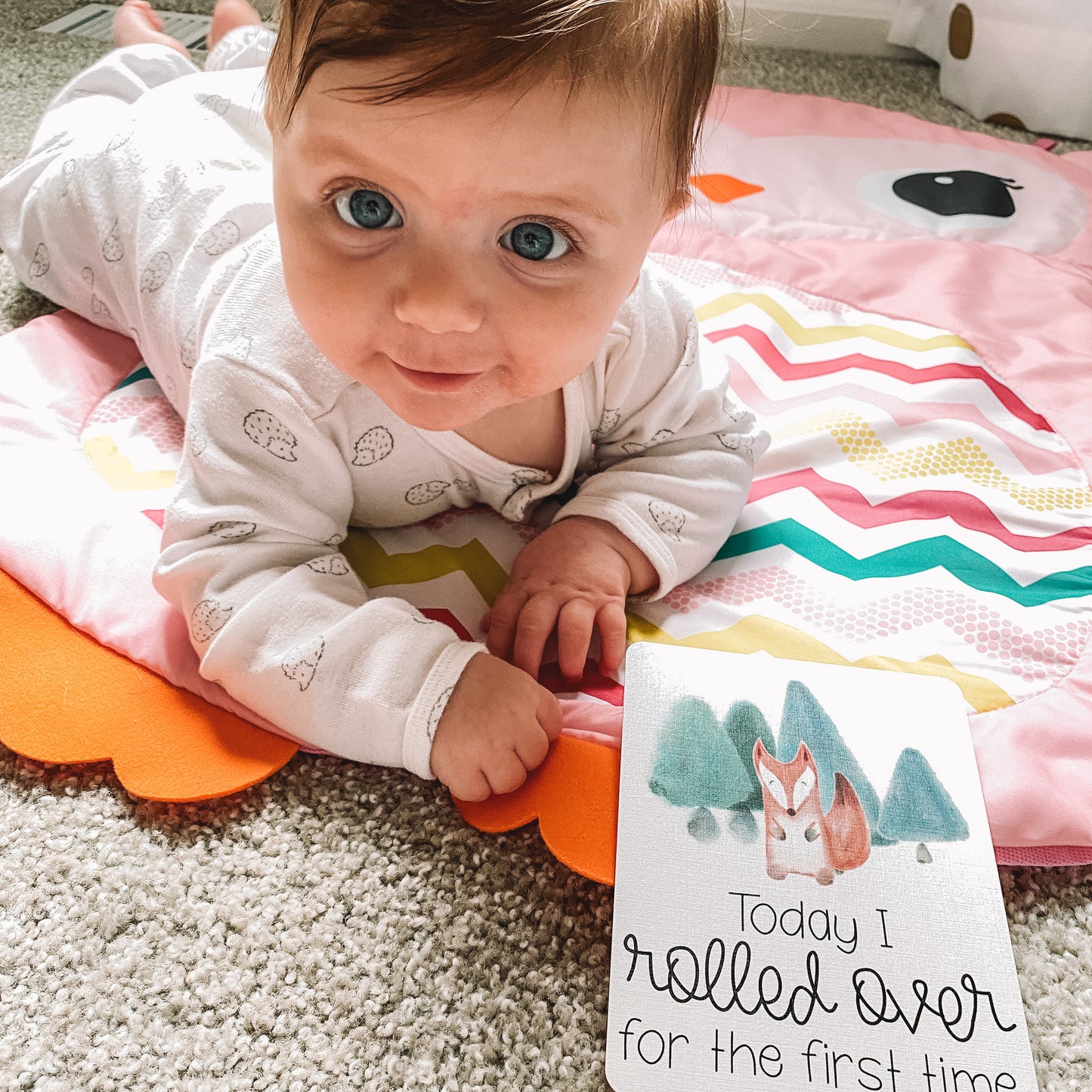 Baby lying on her tummy with the today I rolled over for the first time card in front of her