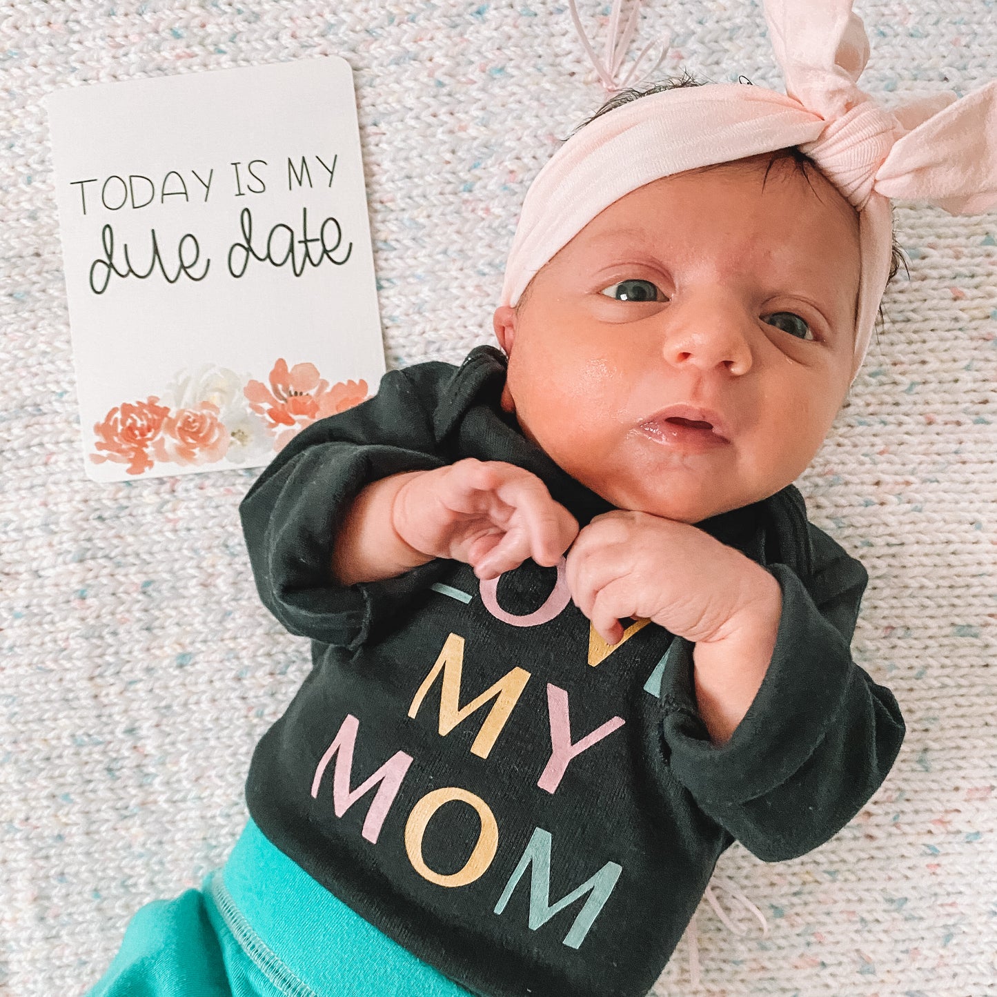 Today is my due date card lying on the floor next to a baby.