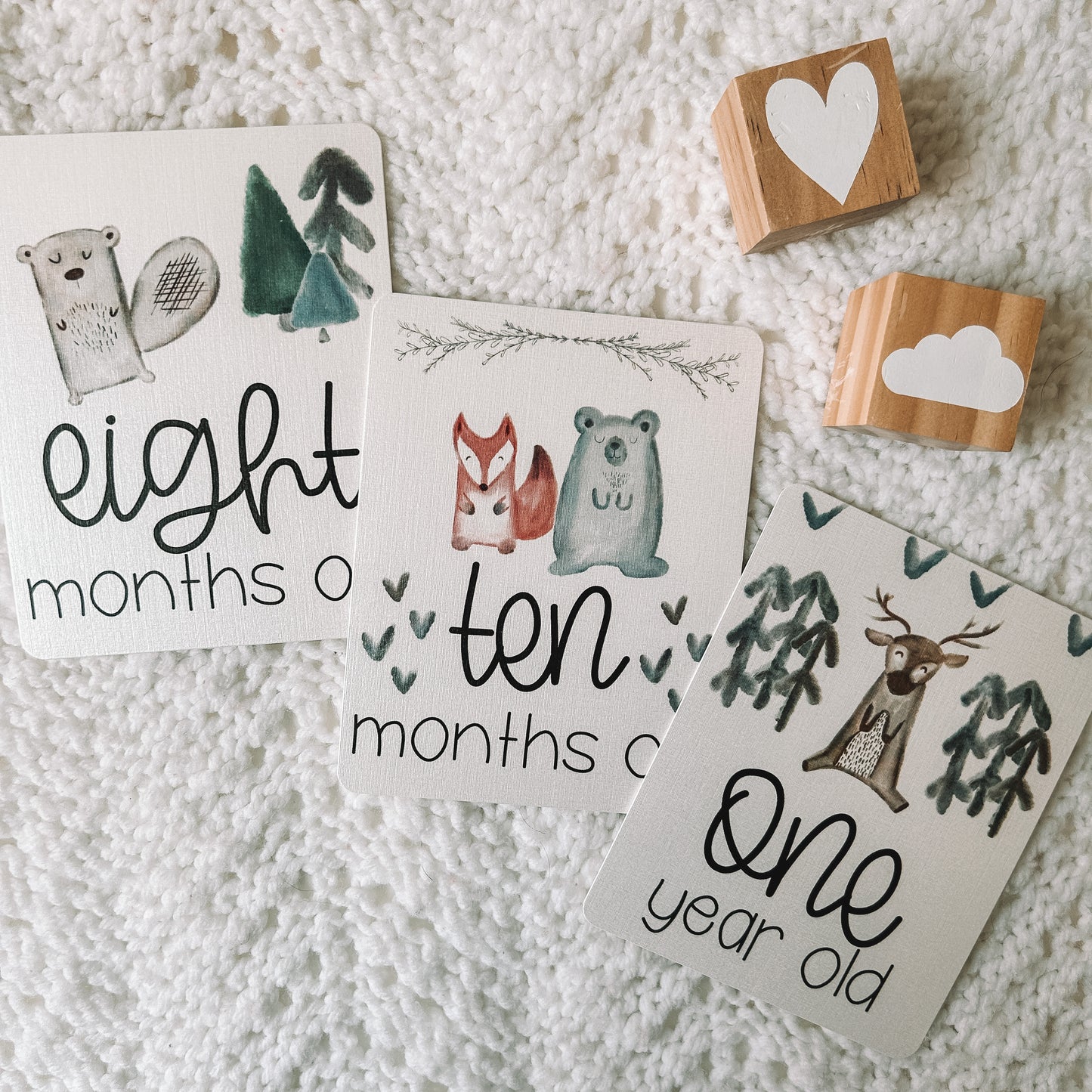 eight months old, ten months old, and one year old card with images of woodland animals, trees, and hearts above the text