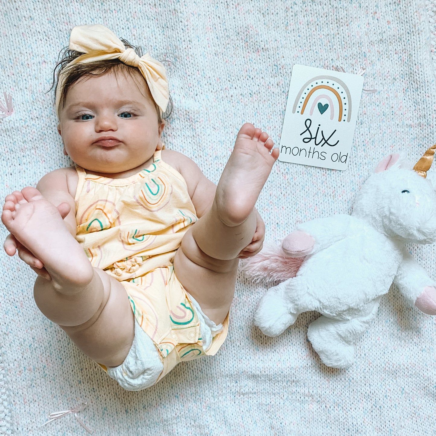 baby lying on a blanket with a six months old card next to her