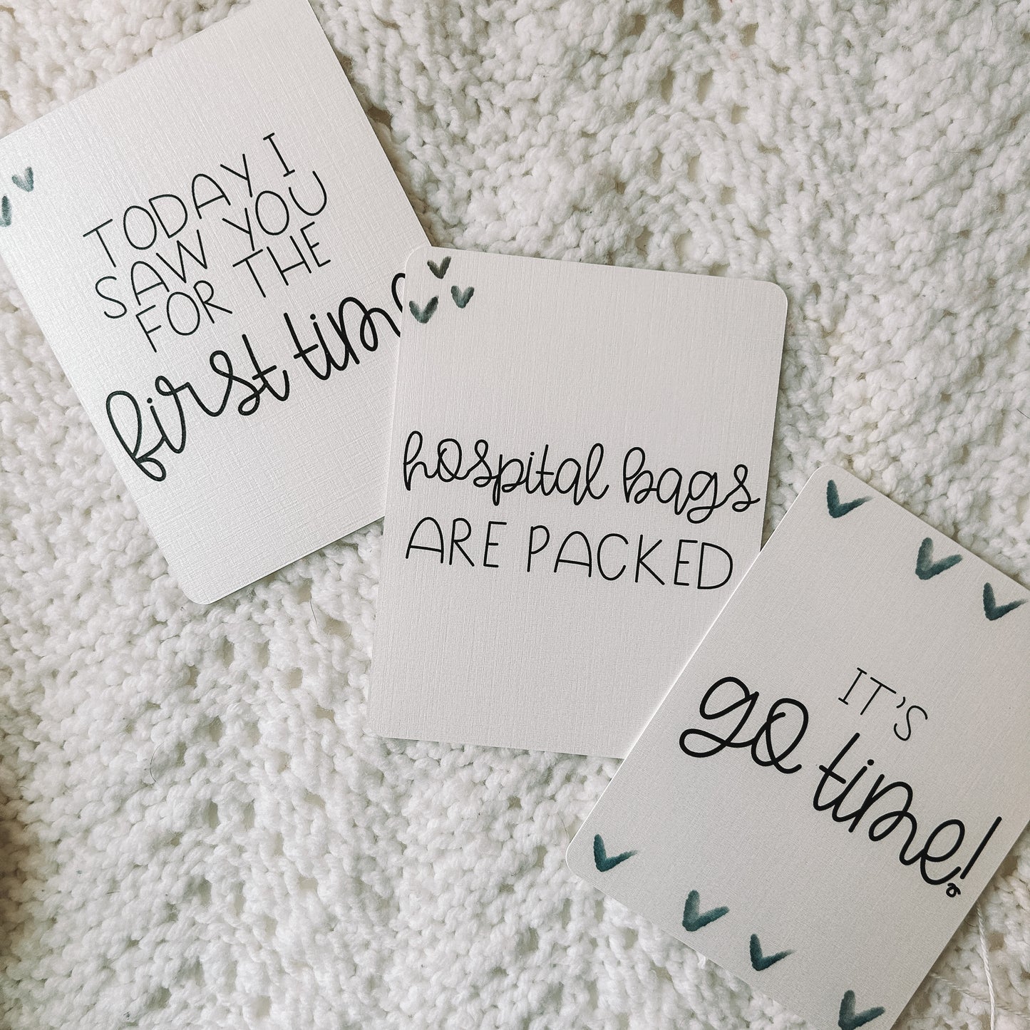 Three milestone cards with black text. Two have hearts in two of the corners of the card and read today today I saw you for the first time and hospital bags are packed. One has hearts lining the top and bottom of the card and reads it's go time.