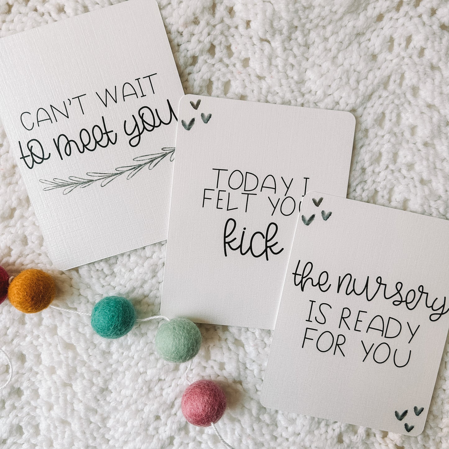 Three milestone cards with black text. One reads can't wait to meet you with a leafed branch beneath. The others have hearts in two of the corners of the card and read today I felt you kick and the nursery is ready for you.