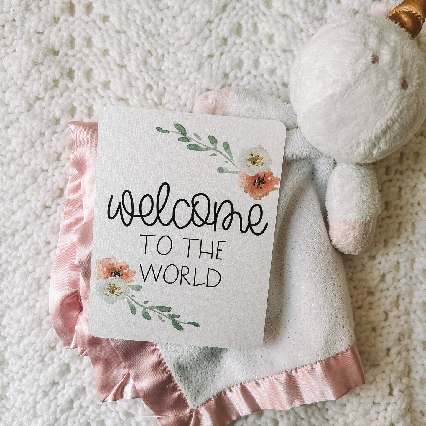 Milestone card reads welcome to the world in black text with flowers around it.