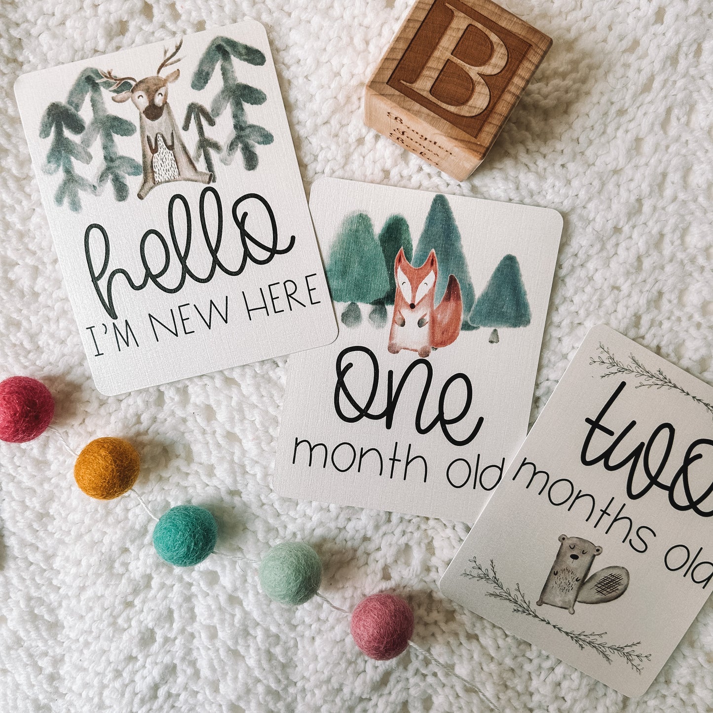 hello I'm new here, one month old, and two months old milestone cards with woodland animals and trees above or below the text