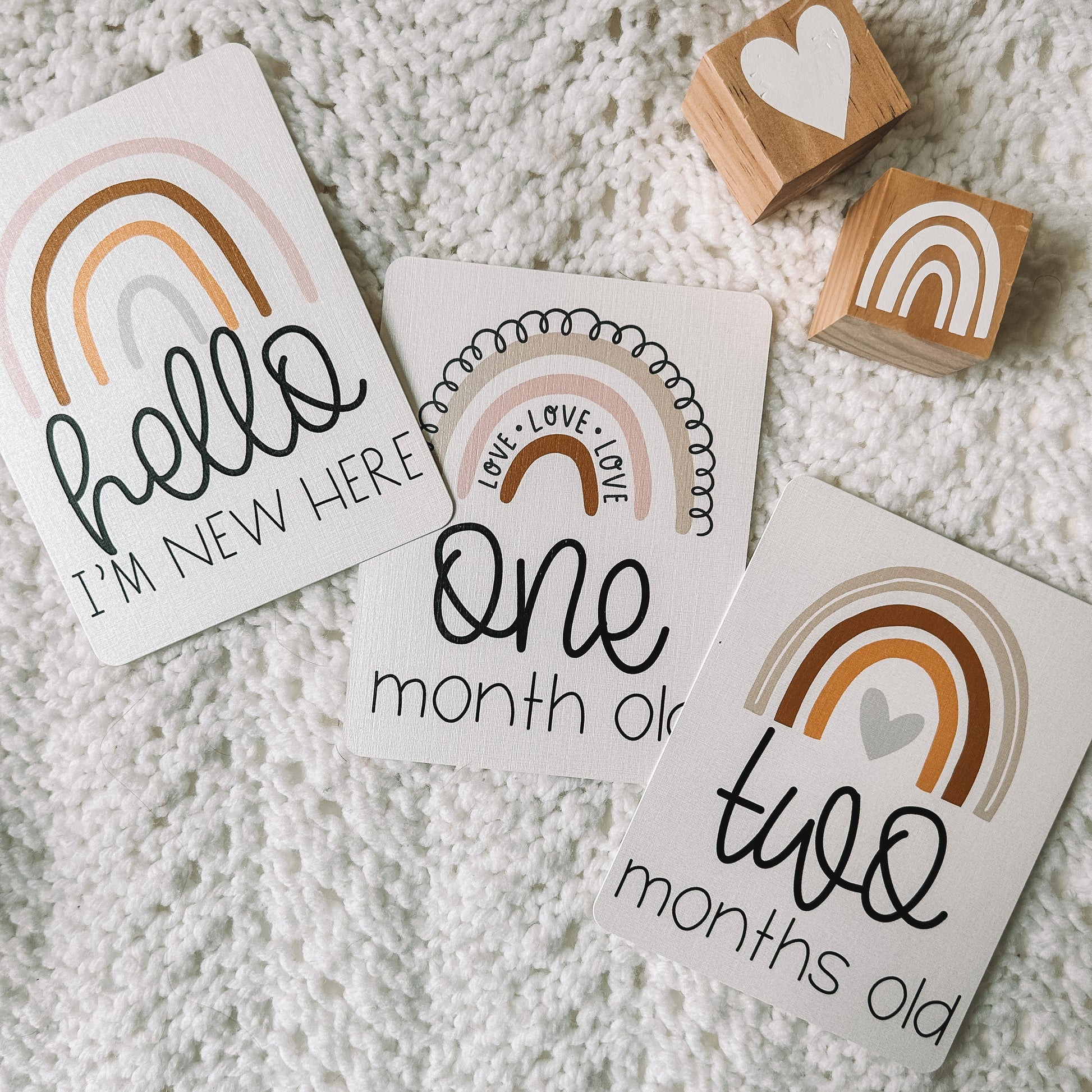 hello I'm new here, one month old, and two months old milestone cards with a rainbow above the text