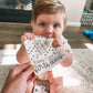 Baby holding a today I got my first tooth milestone card with a beaver and blue polka dots above the text