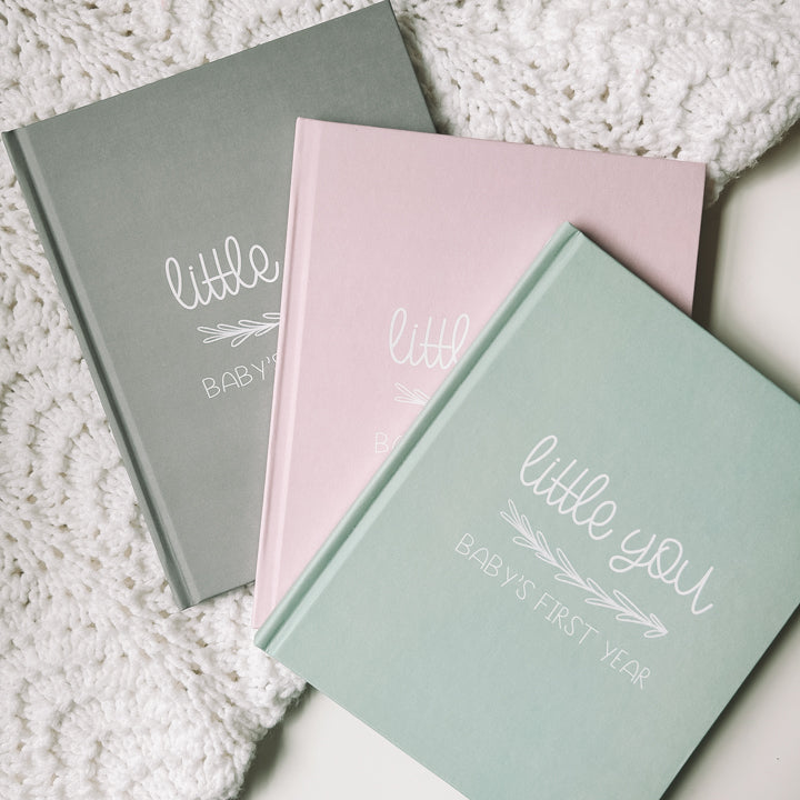 The baby book is available in three colors which are grey, blush pink, and sage green. All feature the title of the book, Little You Baby's First Year, printed in white ink.