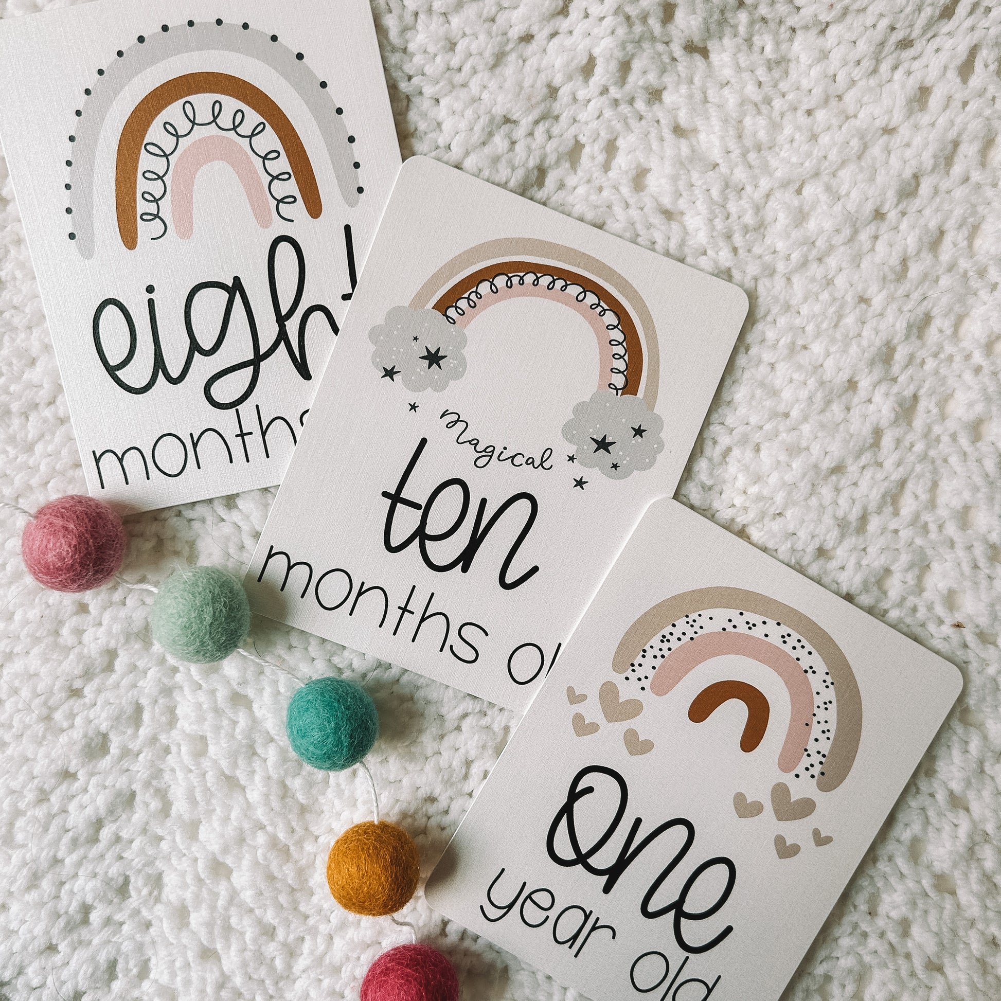 eight months old, ten months old, and one year old card with a rainbow above the text