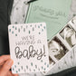 We're having a baby milestone card held over a pregnancy journal and ultrasound photos.