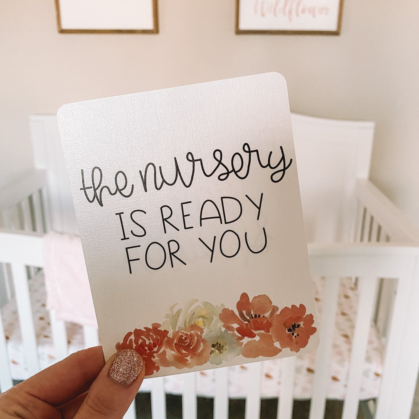 Milestone card with black text that read the nursery is ready for you held in front of a crib.