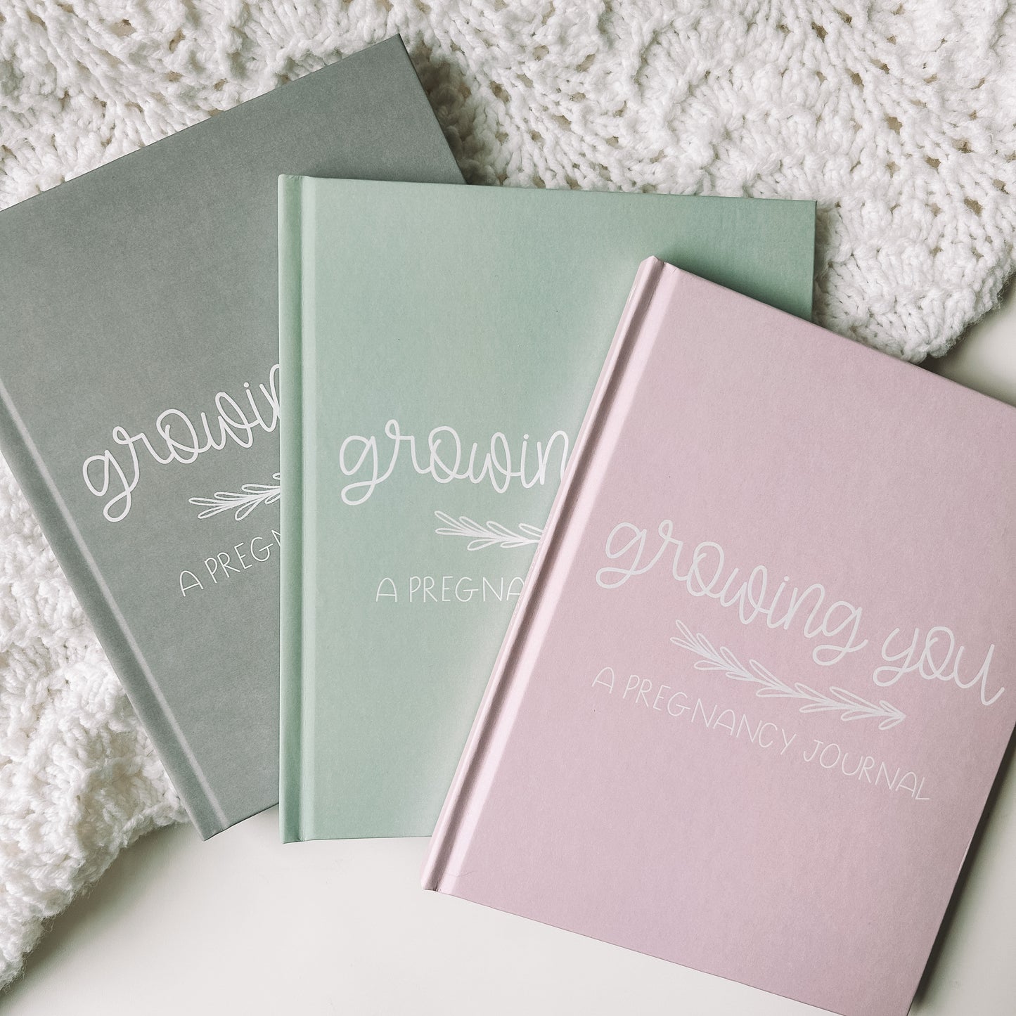 Grey, green, and pink hardcover memory books titled Growing You A Pregnancy Journal in white text.