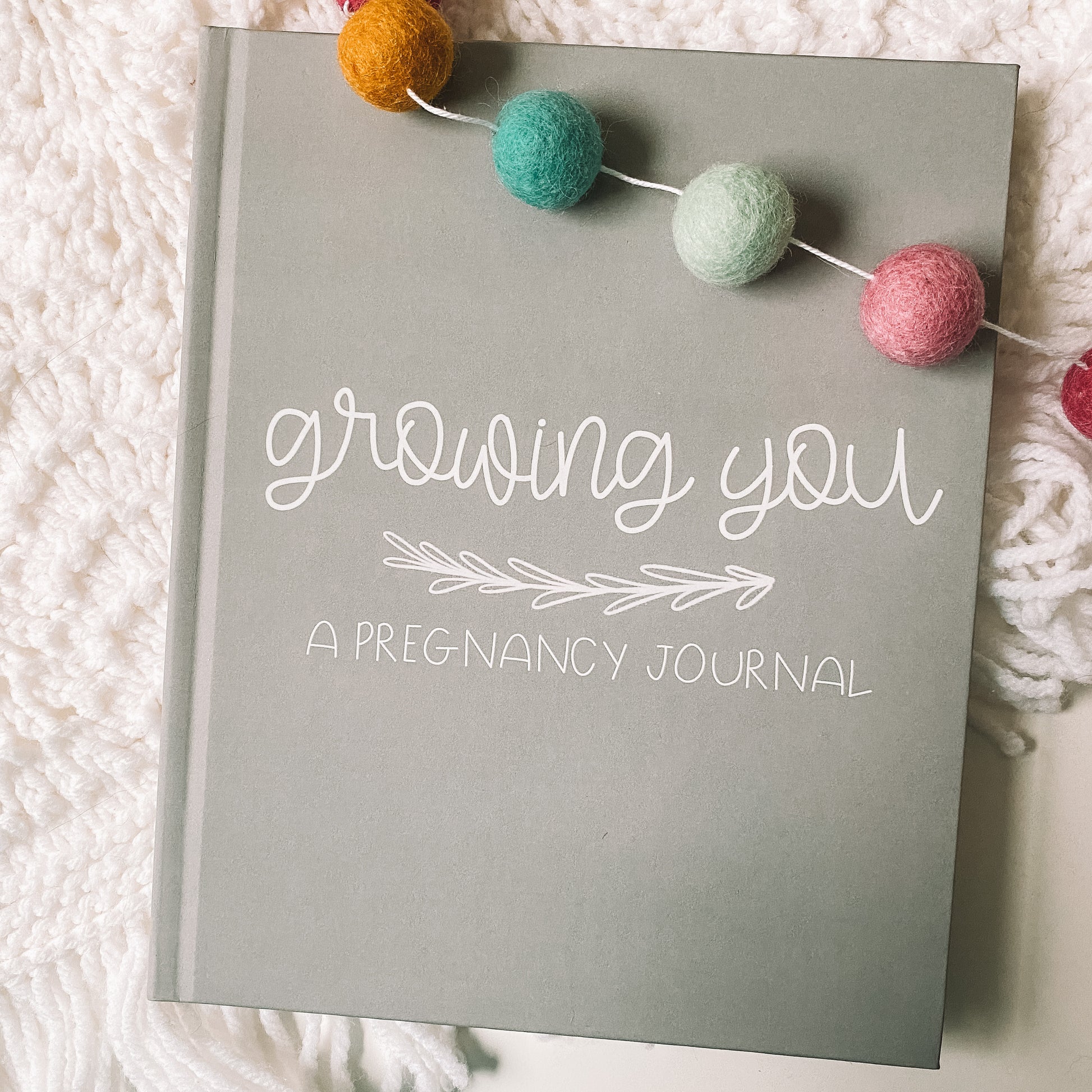 Grey hardcover book with white text titled Growing You A Pregnancy Journal