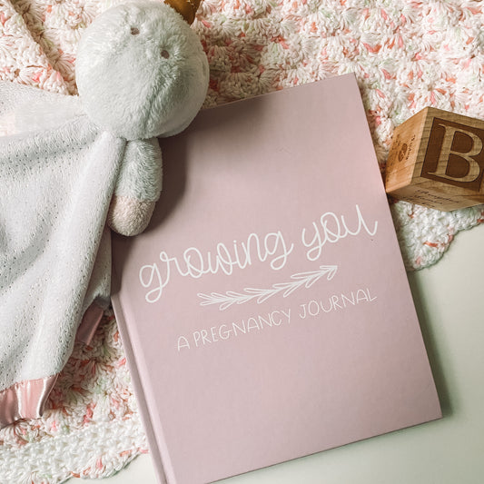 Pink hardcover book with white text titled Growing You A Pregnancy Journal
