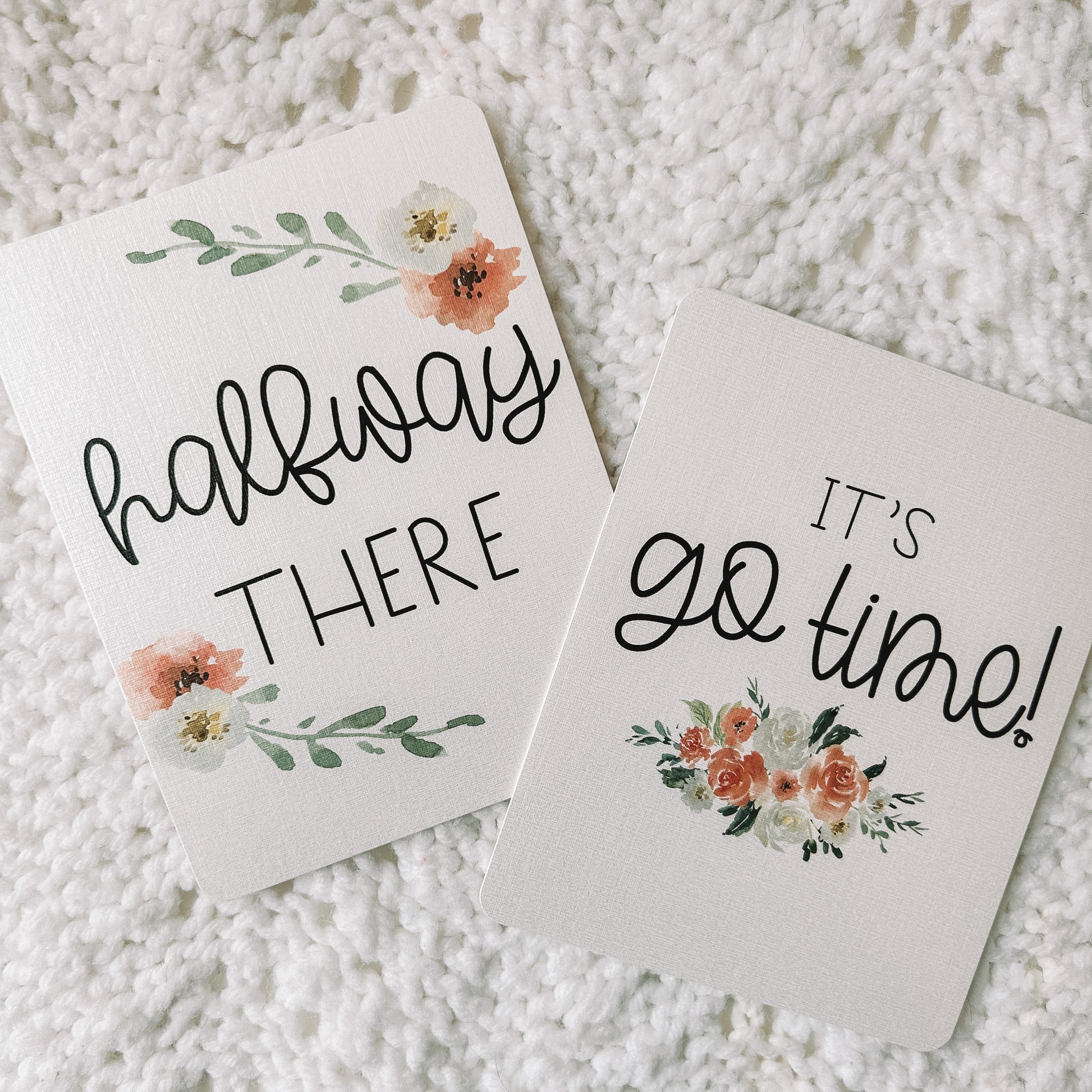 Two milestone cards. One reads halfway there with flowers around it and the other reads it's go time with a floral bouquet beneath it.