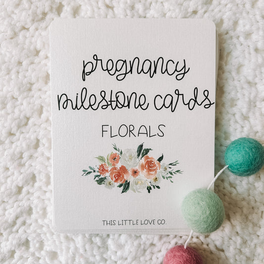 Card with black text that reads pregnancy milestone cards florals. There is an image of a floral bouquet underneath and the text This Little Love Co at the bottom of the card.