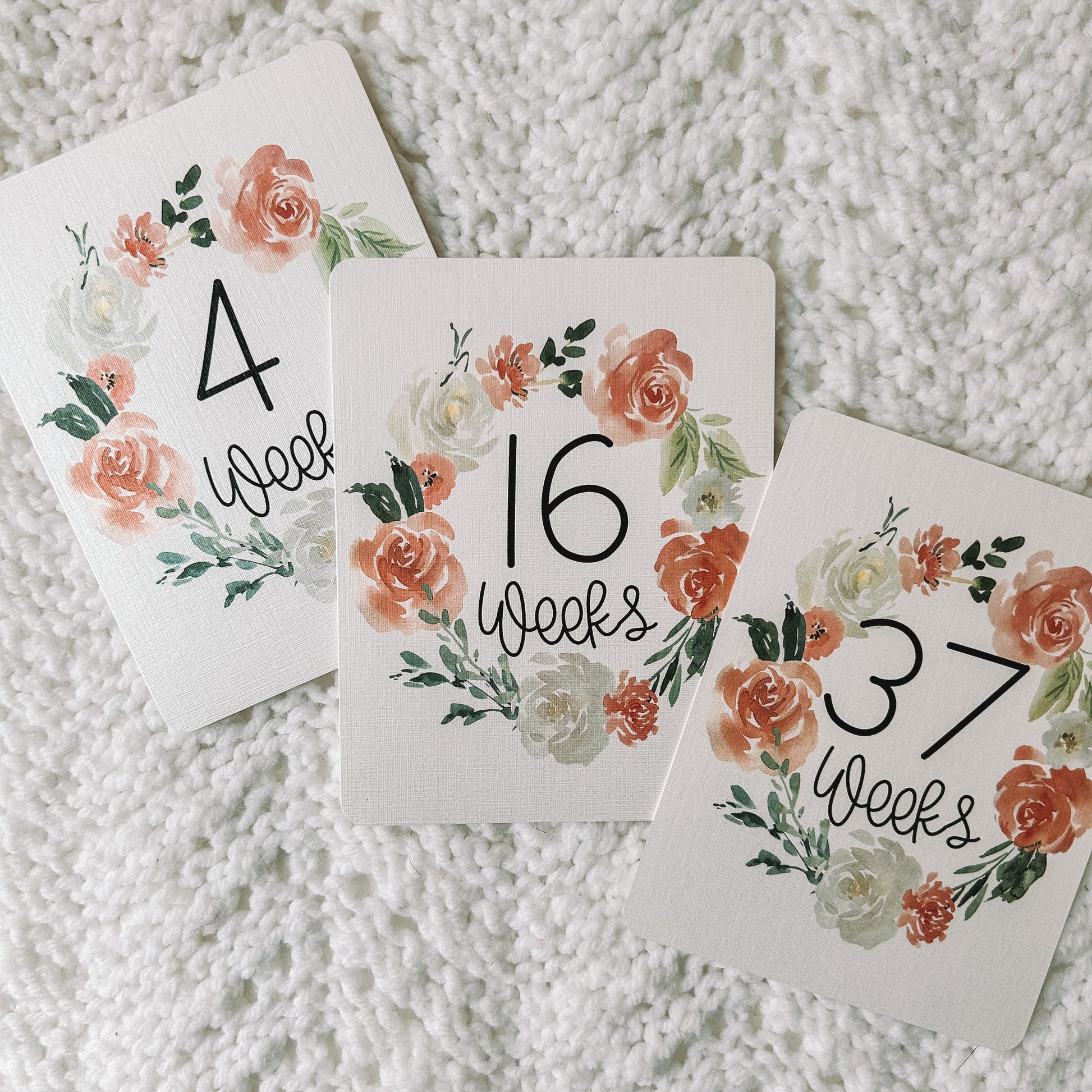 Three cards that read 4 weeks, 16 weeks, and 37 weeks with a floral wreath around the black text.