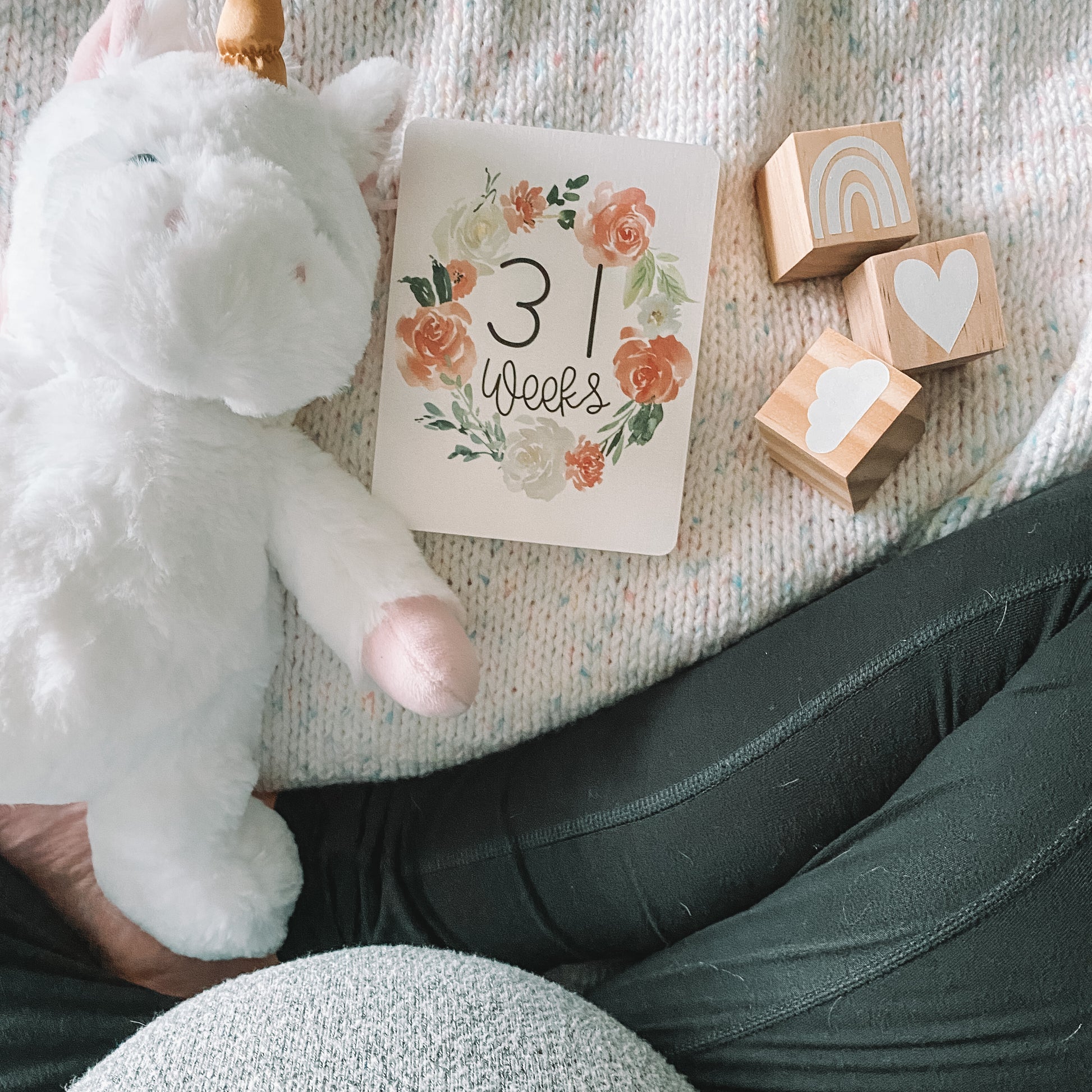 View of pregnant belly with a 31 week milestone card, unicorn stuffed animal, and blocks laid on a blanket in front.