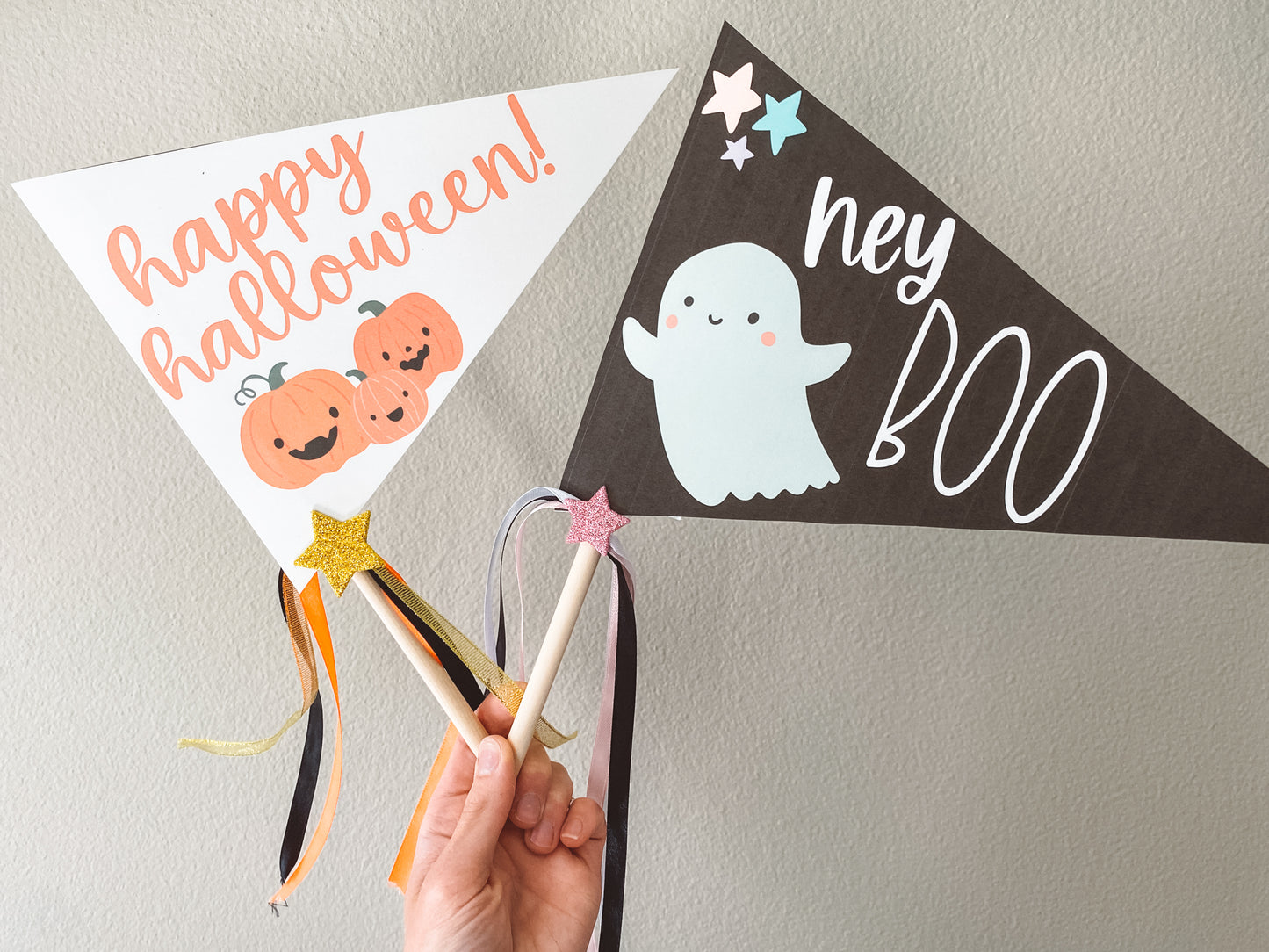 Happy Halloween flag is white with orange text and three orange pumpkins below the text. Hey Boo flag is black with white text and a bluish white ghost. Three stars in the upper left corner. Both on rods with ribbon.