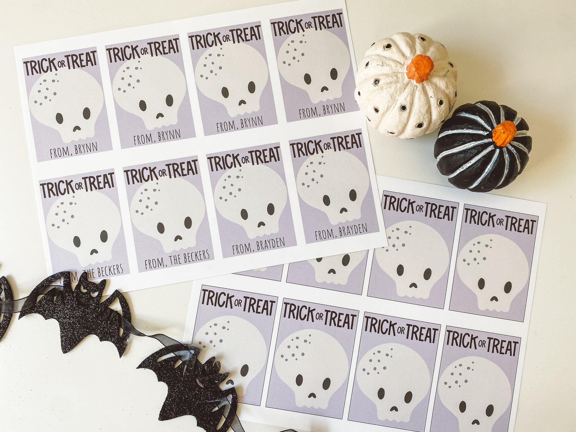 Trick or treat gift tags displayed as they look when printed. 8 tags fit on an 8.5 by 11 inch page. Trick or treat tags have a purple background with cute white skull. Two sheets are displayed. One has the gift giver's name printed and one does not