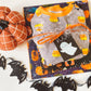 Book and Halloween pajamas wrapped up with yarn with a Boo gift tag attached. Orange pumpkin and black bats complete the flat lay.